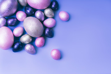 Colored painted pearl chicken and quail eggs of pink, silver, golden and blue color on a light blue pastel background. Minimalistic creative classic easter festive flat lay. Copyspace for text