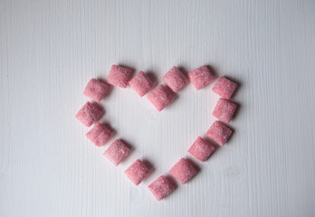 Lots of pink sugar candies on a white wooden background in the shape of a heart