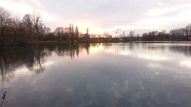 Placid lake water and reflections with sunset at background