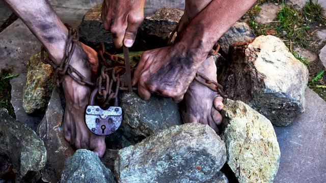 Man in captivity. A slave in iron chains is trying to free himself. A scene from the life of a slave. The symbol of slave labor. Hands and feet in chains. Breaking chains