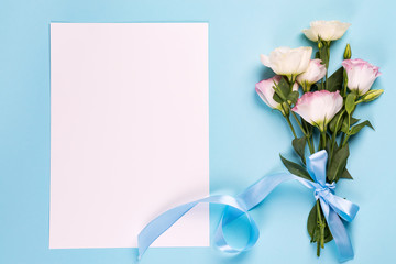 Eustoma flowers with paper sheet on a blue background, top view. Valentines day, birthday, mother or wedding greeting card
