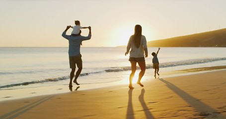 Happy parents with young children playing airplane running and flying on the beach joyfully, adventurous family on vacation - Powered by Adobe