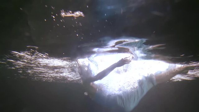 brunette falls into the black water. silvery waves run across the surface, blue fabric ripples. the girl slowly emerges