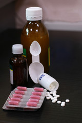 white tablets and vial with syrup lie on a black shelf