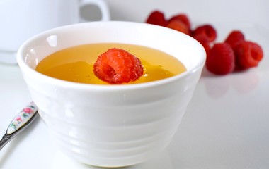 in a white bowl with honey lies one raspberry
