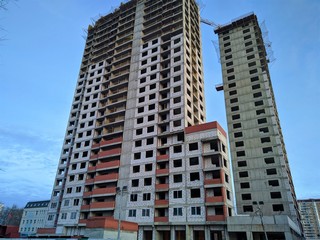 Fototapeta na wymiar Construction of a multi-storey monolithic house of gray concrete against the blue sky