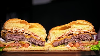 Cut craft burger is cooking on black background in black food gloves. Consist: sauce, lettuce, tomato, red onion, pickle, cheese, bacon, air bun and marbled meat beef. Not made ideal. Looks real