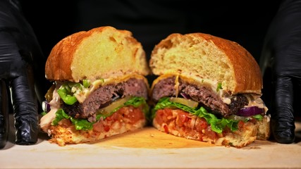 Cut craft burger is cooking on black background. Consist: red sauce salsa, lettuce, red onion, pickle, cheese, chilli green pepper, air bun and marbled meat beef. Not made ideal. Loving hand made.