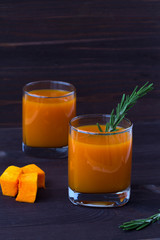 detox cocktail. two glasses of fresh juice of pumpkin with sprig of rosemary, slices of ripe pumpkin on dark wooden background. vertical orientation.