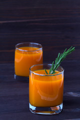 detox cocktail. two glasses of fresh juice of pumpkin, carrot or orange with sprig of rosemary on dark wooden background. vertical orientation.