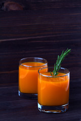 detox cocktail. two glasses of fresh juice of pumpkin, carrot or orange with sprig of rosemary on dark wooden background. vertical orientation.