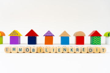 Wooden block with letters saying "Immobilienkredit" (German for real estate loan) in front of colorful toy houses
