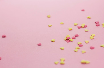  falling yellow and pink heart-shaped confectionery confetti on a pink background copy space.
