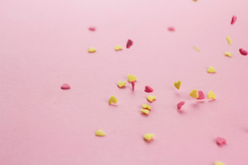  falling yellow and pink heart-shaped confectionery confetti on a pink background copy space.
