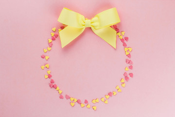  wreath of yellow and pink confetti in the shape of hearts and a yellow bow on a pink background copy space.