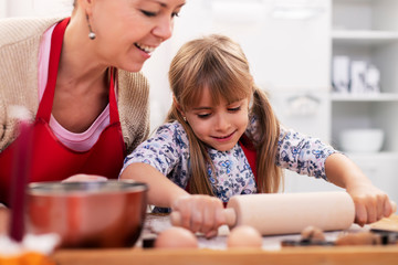 Cute little girl stretching the cookie dough at the kitchen table with her mother