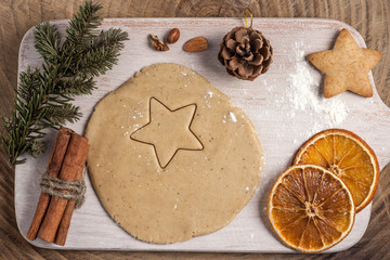 Christmas homemade baking background: ginger dough rolled out on a wooden board, cookies, cinnamon and slices of dried oranges. Top view, flat lay, copy space.