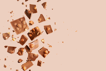 Flying in the air broken bar of milk chocolate with nuts and flakes on pastel pink background. ...