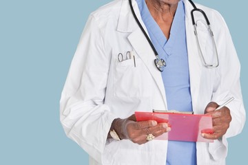 Midsection of male doctor writing on clipboard over light blue background