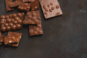 The chunks of broken different chocolate bars with nuts on the black stone surface with space for text. Background with chocolate. Sweet food photo concept.