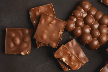 The chunks of broken different chocolate bars with nuts on the black stone surface with space for text. Background with chocolate. Sweet food photo concept.