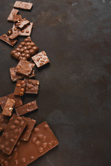 The chunks of broken different chocolate bars with nuts on the black stone surface with space for text. Background with chocolate. Sweet food photo concept.