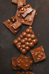 The chunks of broken different chocolate bars with nuts on the black stone surface with space for text. Background with chocolate. Sweet food photo concept.