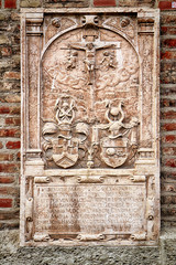 Antique sculpted tombstone  of the 17th century with coat of arms and crucifixion scene encased in the exterior wall of the Frauenkirche cathedral in Munich