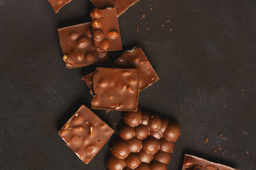 The chunks of broken different chocolate bars with nuts on the black stone surface with space for text. Background with chocolate. Sweet food photo concept.