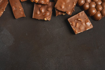 The chunks of broken different chocolate bars with nuts on the black stone surface with space for text. Background with chocolate. Sweet food photo concept.