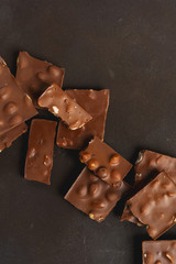 The chunks of broken different chocolate bars with nuts on the black stone surface with space for text. Background with chocolate. Sweet food photo concept.