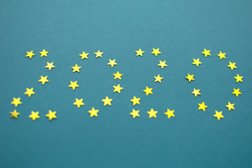 Happy New 2020 Year background. Number 2020 from gold stars confetti at blue background.
