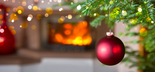 Photo of burning fireplace next to decorated Christmas tree with red bauble.