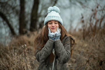 Emotion photo. Cute white emotional caucasian teen girl in a blue hat stands in the park in cold autumn weather.