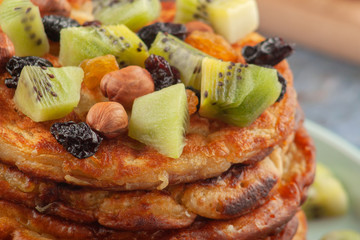 On the table is a dish with pancakes, honey, kiwi, nuts and raisins.