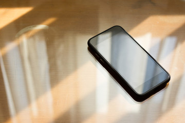 Mobile phone on a wooden table by the window and copy space.