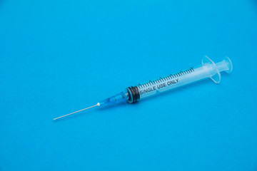 An empty disposable syringe lies on a blue background. Medicine concept. Side view. Selective focus.