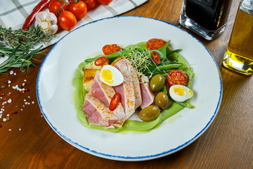 Chef's reinvention of Nicoise salad with fresh tomatoes, asparagus, chili peppers, olives, quail eggs and fried tuna. Traditional french salad. Close up view on healthy seafood salad