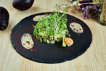 Fashionable Russian salad Olivier with avocado and shrimp on a black slate blackboard. Close up view on tasry seafood salad