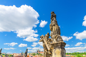 Fototapeta na wymiar Madonna and Saint Bernard statue on Charles Bridge Karluv Most over Vltava river with Prague Castle, St. Vitus Cathedral in Hradcany district, blue sky white clouds background, Bohemia, Czech Republic