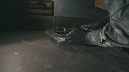 Forge workshop. Smithy. Worker in a welding hood helmet welds a part by electric welding. Sparks are reflected in the protective screen. Blacksmith makes iron product for manufacture. Slow motion.