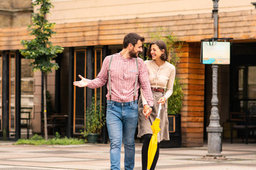 A man and a woman on the street walking and talking holding hands with fingers entwined,smiling.