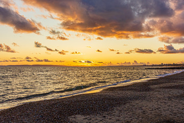 A view of a stony beach at sunset with crashing waves and ecume under a majestic yellow cloudy stormy sky