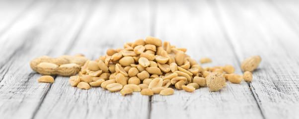 Wooden table with salted and roasted peanuts (close-up shot)