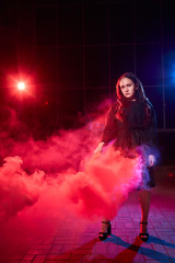 Teenage chubby girl with colored smoke torch in hand during photoshoot with colored smoke at night and black background