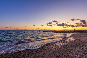 A view of a stony beach at sunset with crashing waves and ecume under a majestic yellow cloudy stormy sky