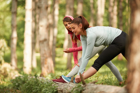 Two beutiful caucasian grils stretching legs and chatting. Fitness in nature concept.