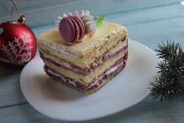 A piece of cake on a platter, a red ball and a branch of spruce on the table.