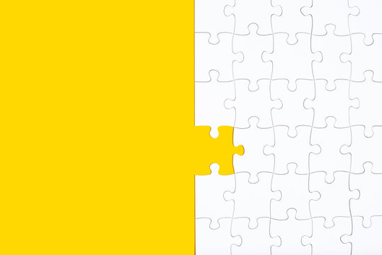 Unfinished white jigsaw puzzle pieces on yellow background