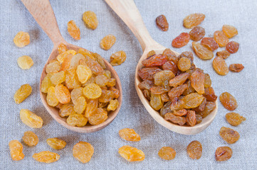 Light and dark raisins in wooden spoons on gray fabric background